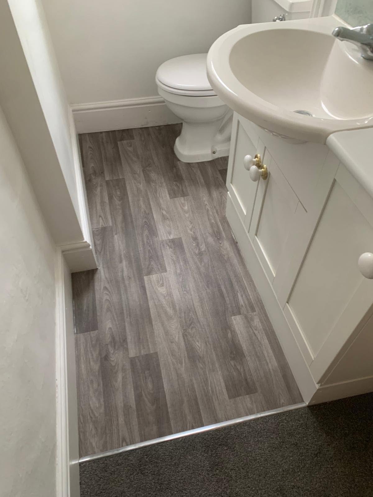 Grey wood-effect vinyl in a bathroom meeting carpet at a threshold strip