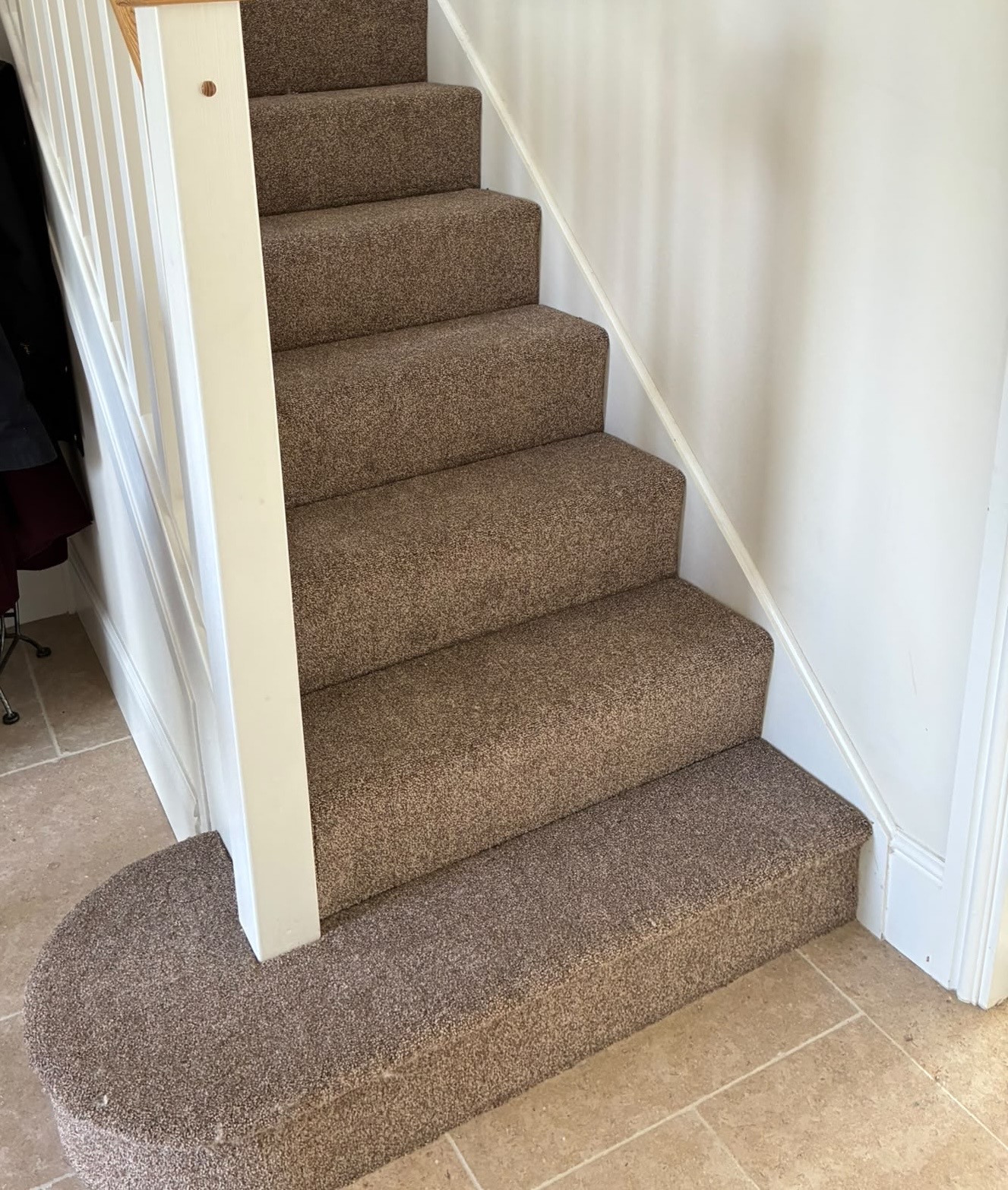 Carpeted stairs with a curved bottom step over a tiled floor